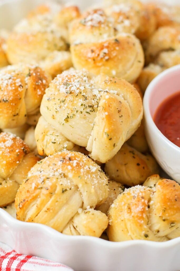 Close Up Of Baked Garlic Knots With A Bowl Of Marinara.