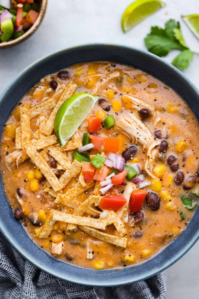 A Serving Of Chicken Fajita Soup, Topped With Tortilla Strips, Diced Tomatoes, And A Lime Wedge.